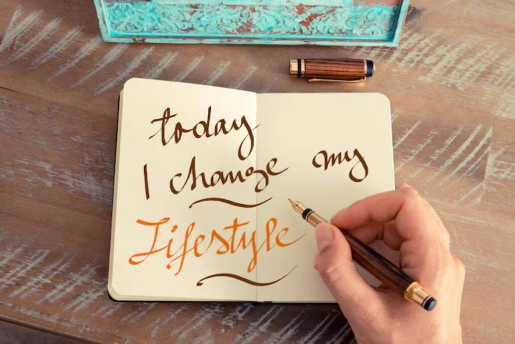 A hand writes 'today I change my lifestyle' in a notebook, alongside a fountain pen and decorative box on a wooden table.