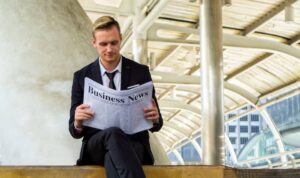 A person in a suit sits on a bench reading a newspaper titled 'Business News' in a modern architectural setting