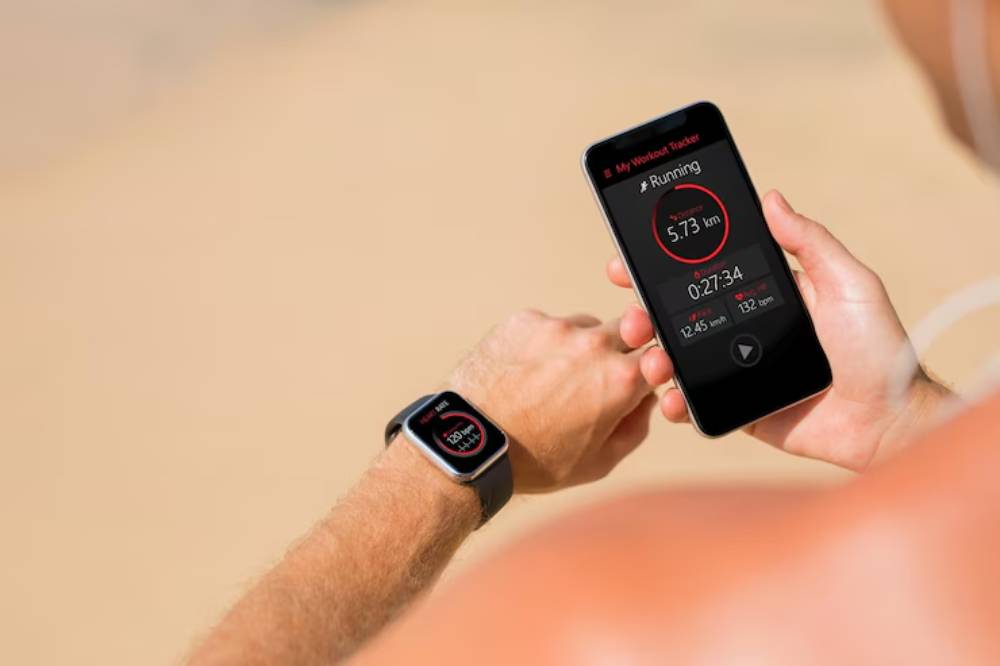 A person checks their running stats on a smartphone and smartwatch, displaying distance, time, and heart rate outdoors.