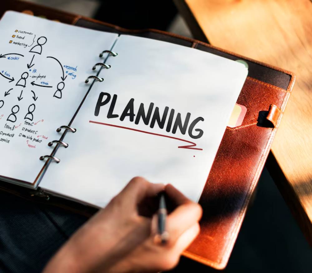 A hand writing in a notebook titled 'PLANNING,' surrounded by sketched diagrams and notes on organization and marketing strategies.