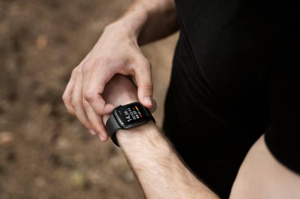 A person checks their smartwatch while outdoors, displaying fitness metrics on the screen. Hands are positioned on the wrist.
