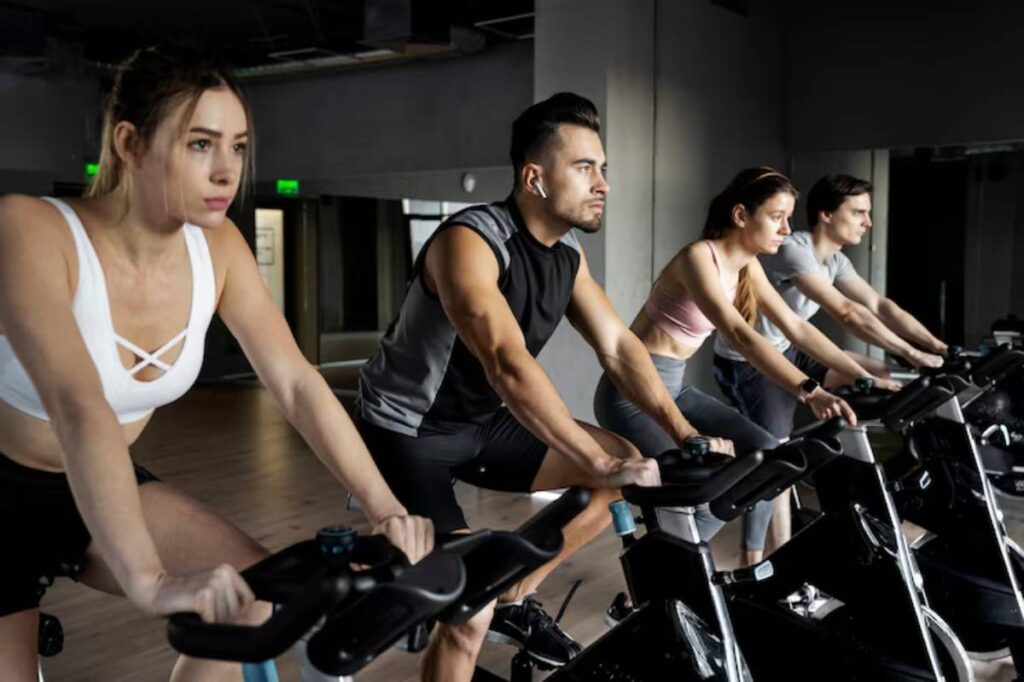 A group of four individuals is engaged in an indoor cycling class, focused on their workout in a modern gym setting.