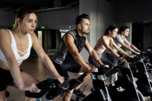 A group of four individuals is engaged in an indoor cycling class, focused on their workout in a modern gym setting.