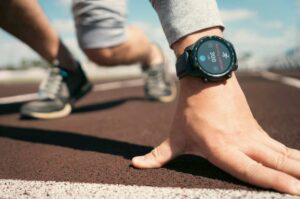 A close-up of a runner's wrist with a sports watch displaying 300 calories burned, reaching towards the running track.