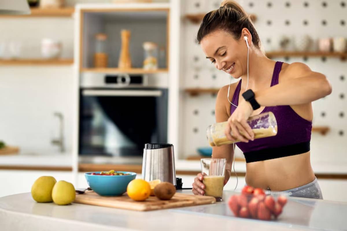 A woman prepares a smoothie in a modern kitchen, pouring it into a glass while surrounded by fresh fruits and a bowl of cereal.